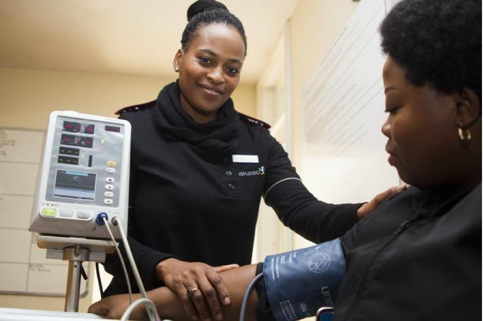 Female nurse smiling while she holds the arm of a patient with a medical device connected