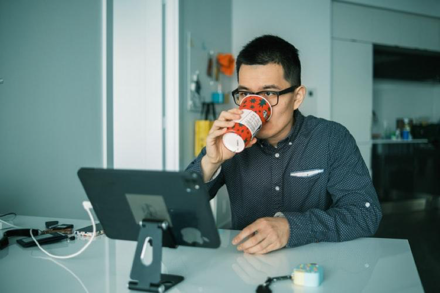 Middle aged Asian man drinking coffe while sitting in front of an iPad on a tripod
